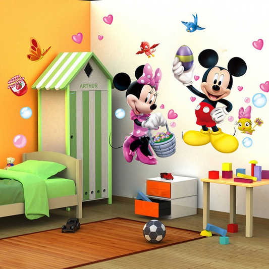 A children's bedroom scene featuring large Mickey Mouse and Minnie Mouse wall decals with Easter-themed elements like hearts, eggs, a butterfly, and a bird. The room includes a bed with green bedding, a green-and-white house-shaped wardrobe, a small table with colorful blocks, and a wooden floor.